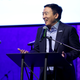 Andrew Yang talks at a podium surrounded by microphones.